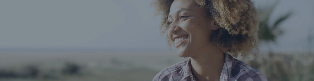 A woman with curly hair and a plaid shirt, outside in a field.