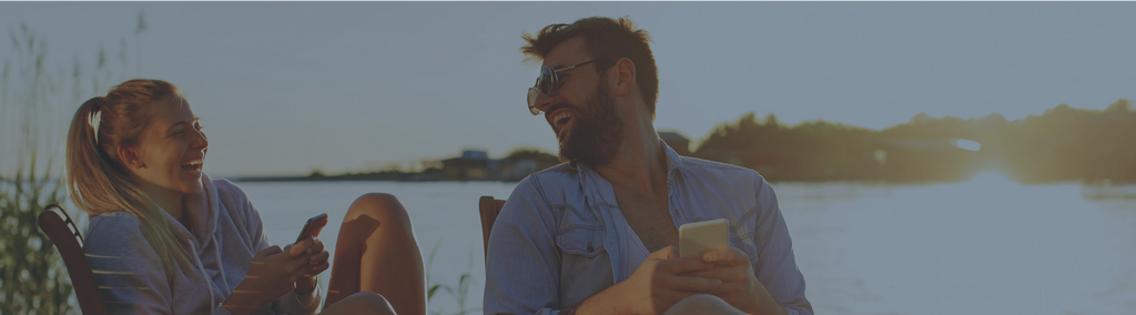 Two people laughing together while sitting outside near a lake.