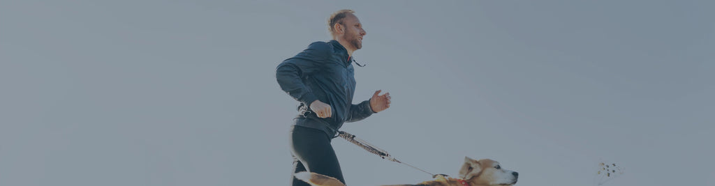 A man running outside with a pet dog on a leash.