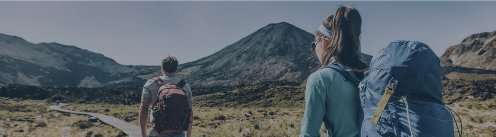 Two people hiking along a trail with mountains in the background.