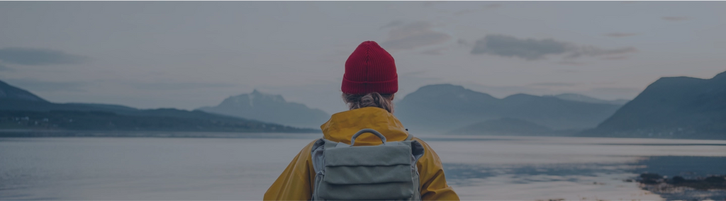 A person wearing a red hat and yellow jacket, looking out over a mountain lake.