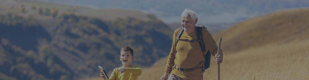 A man with white hair and a young boy hiking together in the mountains.