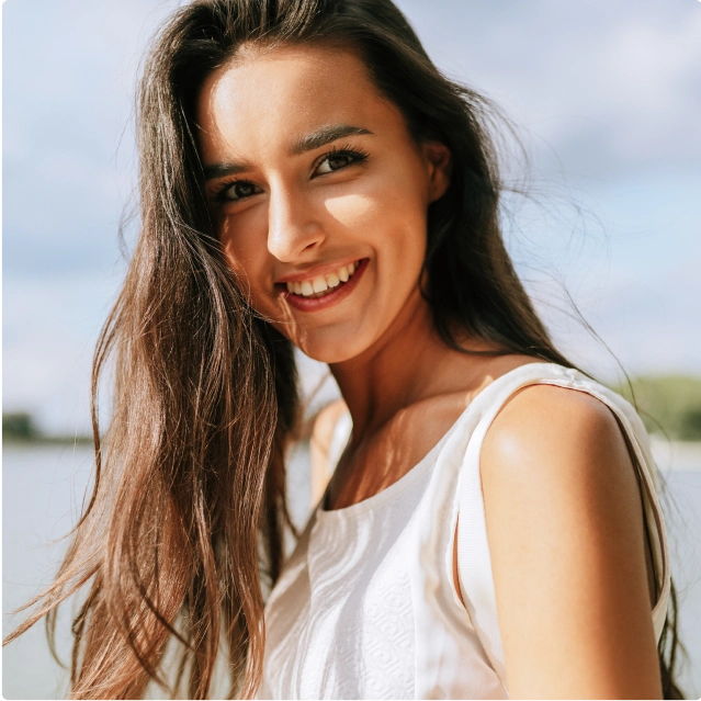 A woman standing outside in the sunshine and smiling at the camera.