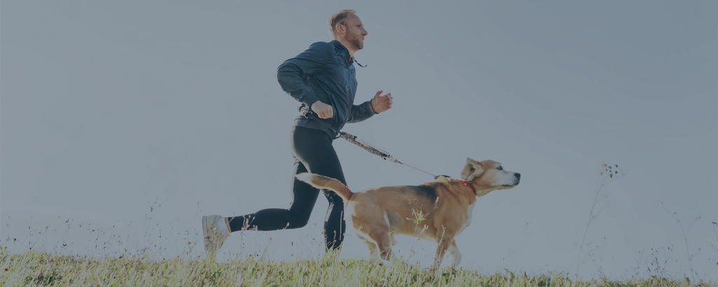 A man in a tracksuit running with a dog.