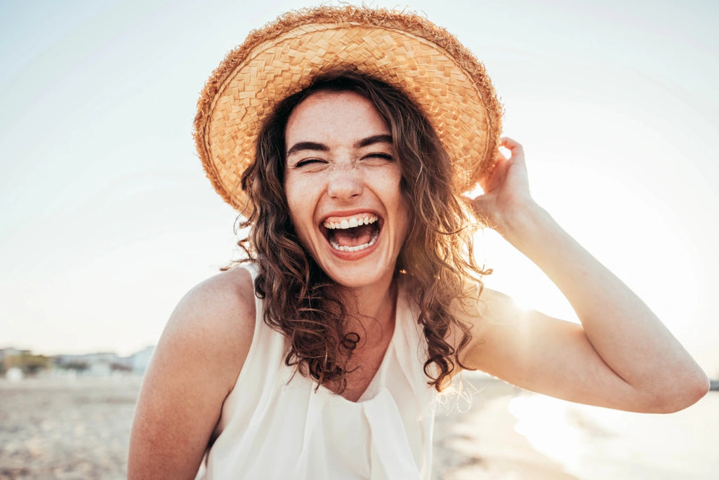 A woman on the beach smiling and wearing a straw hat.