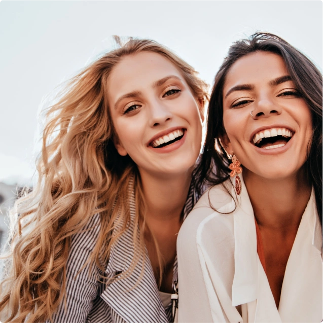 Two women standing together outside and smiling at the camera.